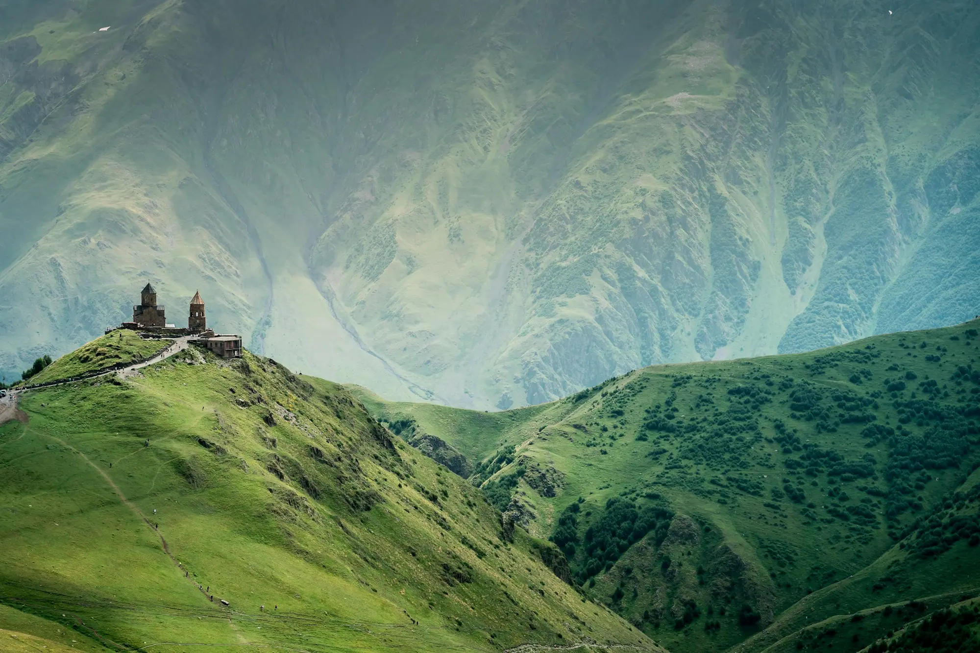 Gergeti Trinity Church on a green ridge in the Caucasus above Stepantsminda